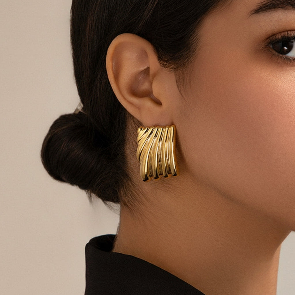Gold earrings worn by a person with a neutral background