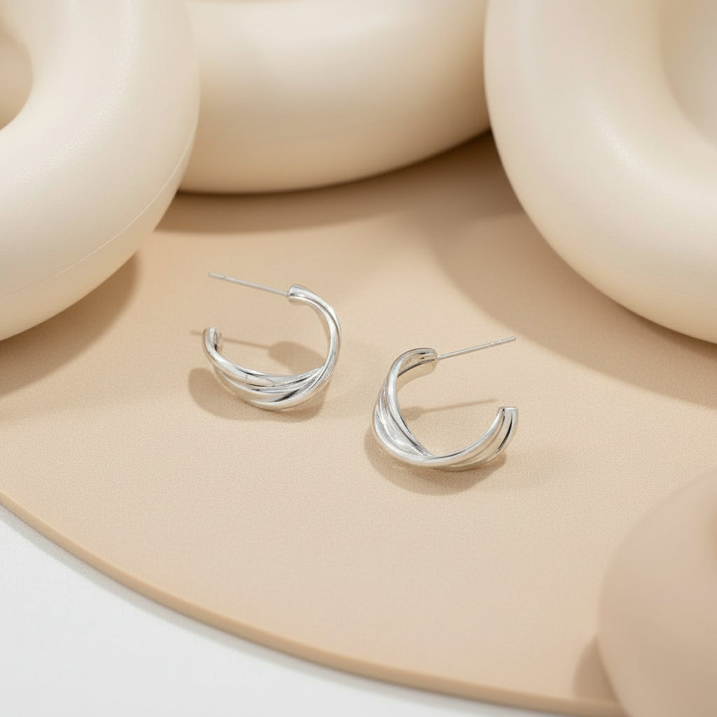 Silver hoop earrings on a white surface with a white bowl in the background