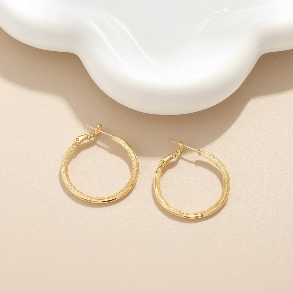 Gold hoop earrings on a white surface with a soft shadow